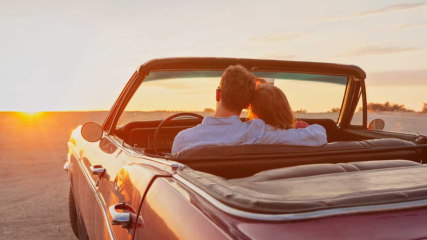 Pärchen sitzt im Oldtimer und schaut den Sonnenuntergang an
