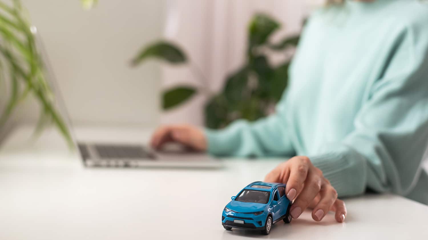 Frau sitzt vor dem Laptop und hat ein Miniaturauto in der Hand