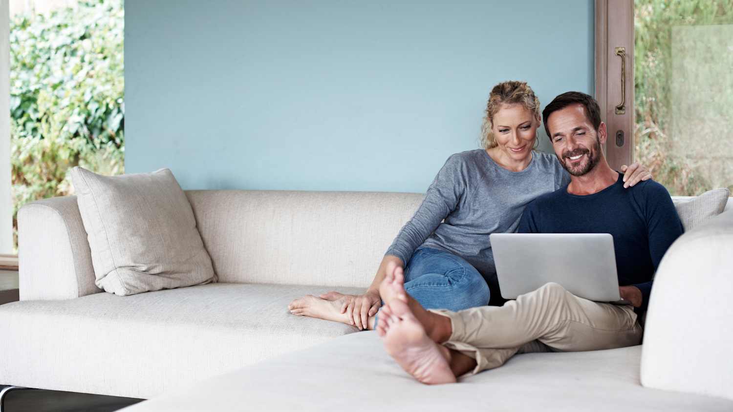 Paar sitzt vor dem Laptop auf dem Sofa und informiert sich online über die ADAC Kreditkarte