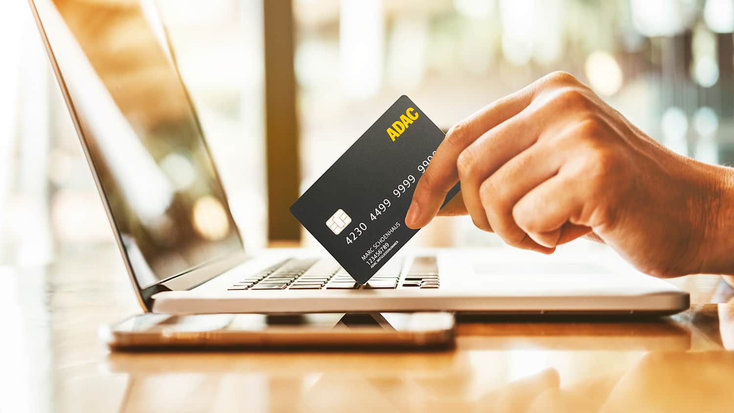 Die ADAC Kreditkarte wird in der Hand gehalten und auf dem Laptop präsentiert