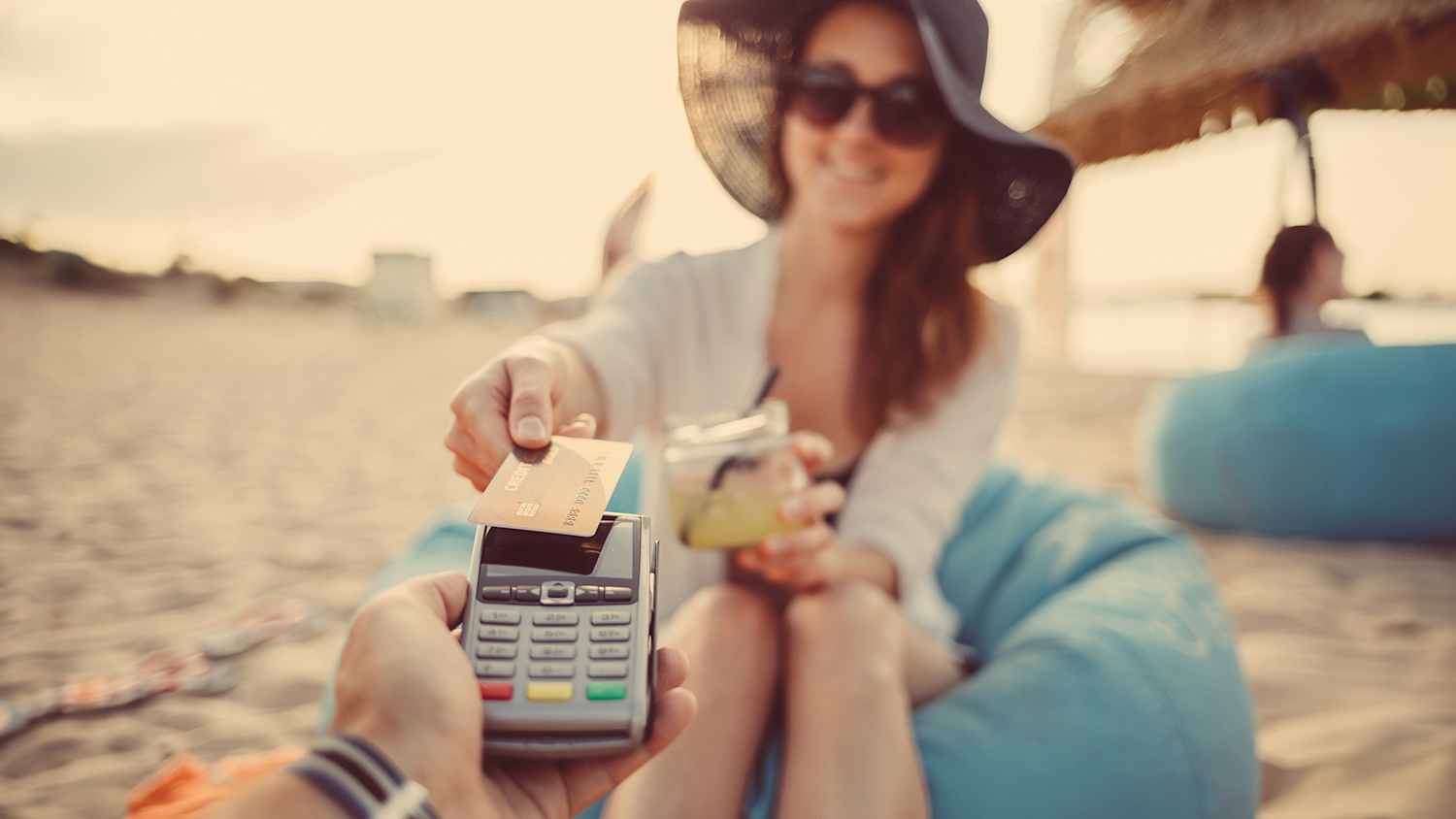 Eine Frau sitzt am Strand und bezahlt ihren Cocktail mit einer debitkarte oder kreditkarte