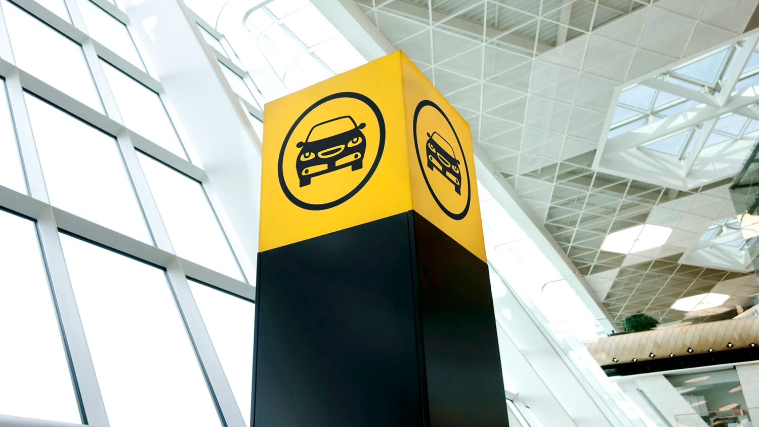 Ein gelbes Schild mit einem Autosymbol in einem großen Gebäude weist auf einen Mietwagenservice hin, der eine gute alternative bei einem Streik der Bahn bietet.