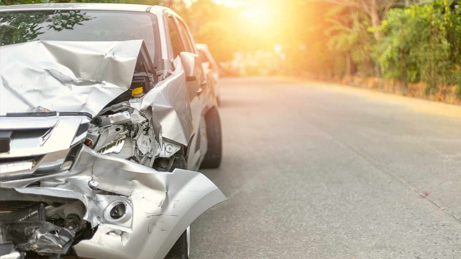 Beschädigtes silberes Auto bei Sonnenuntergang nach einem Unfall mit dem Leasingauto