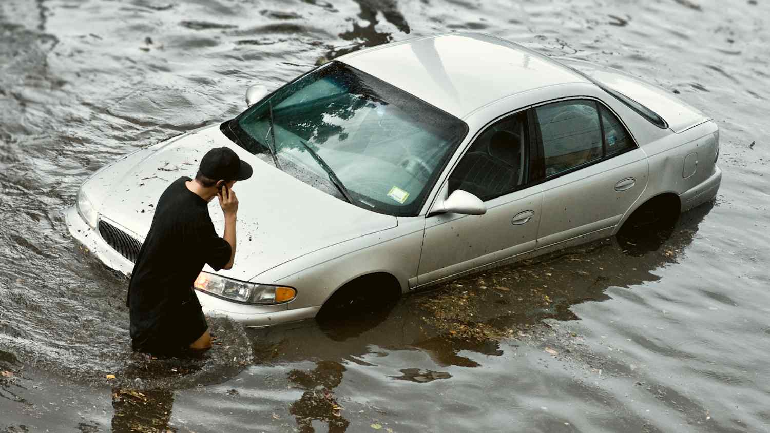 Eine Person telefoniert während sie im Hochwasser ihr Auto betrachtet