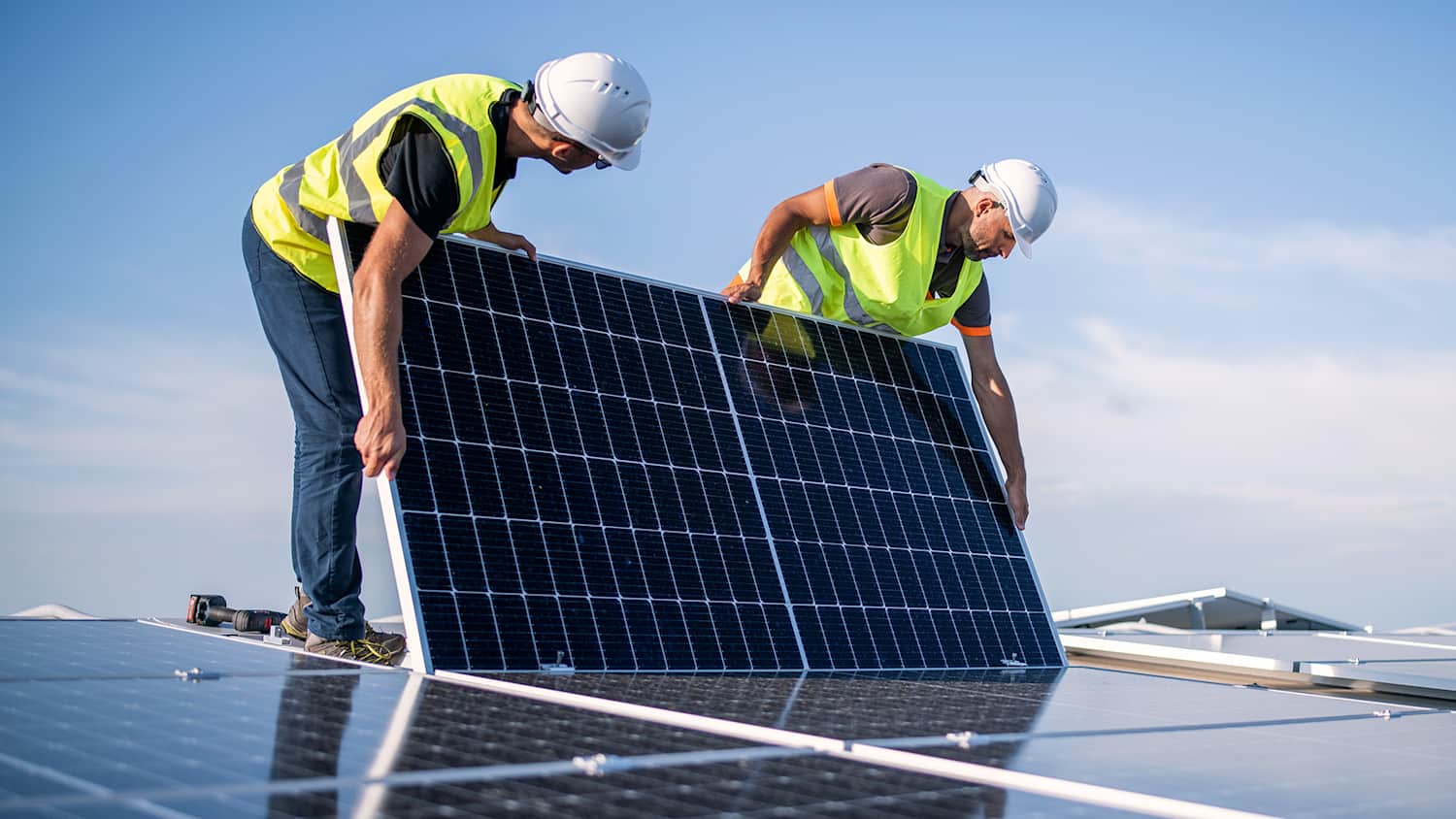 Zwei Handwerker installieren eine PV-Anlage auf einem Dach