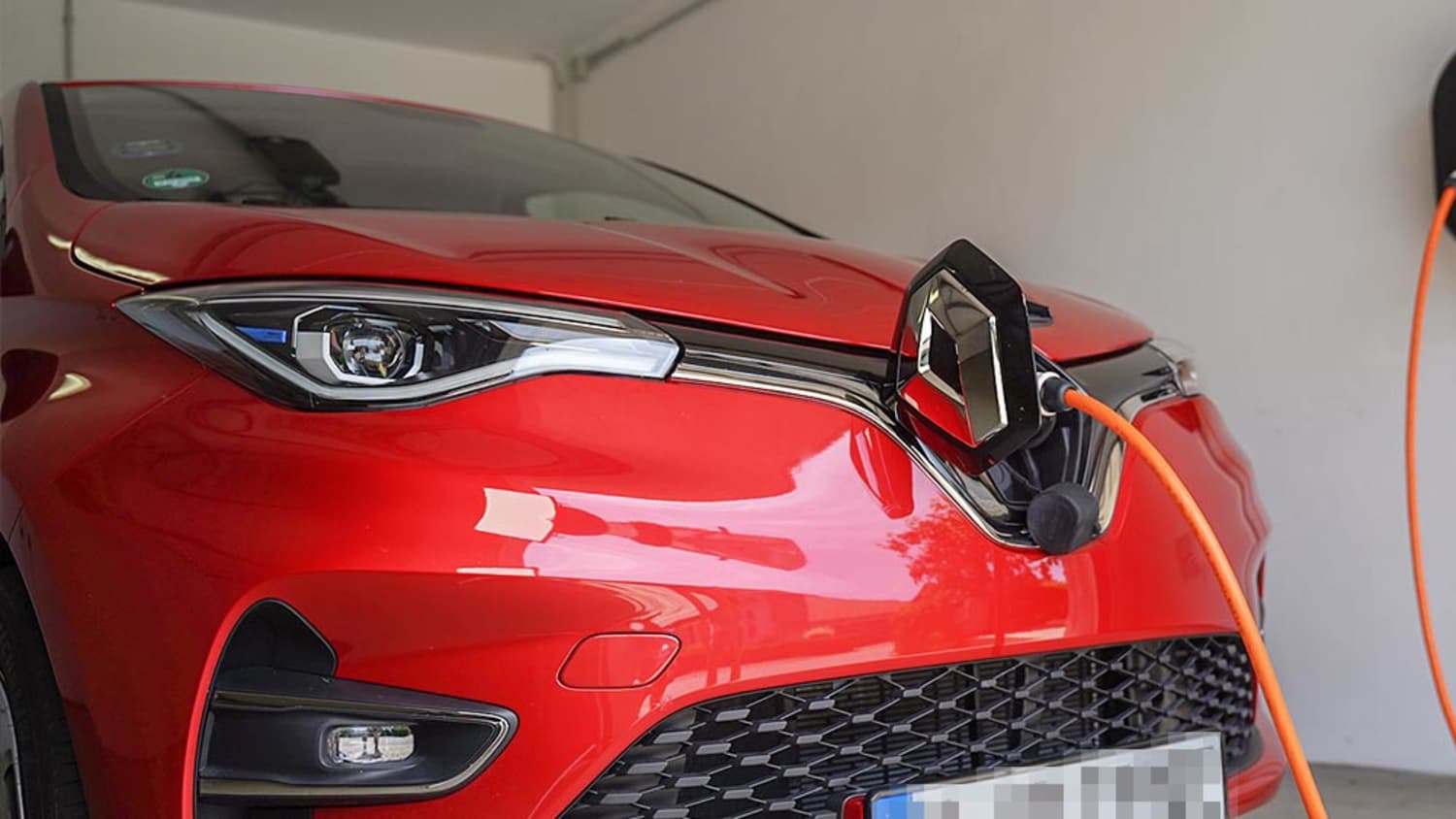 Ein rotes E-Auto wird an einer Wallbox in der Garage geladen, denn nun kann man Zuhause E-Autos laden