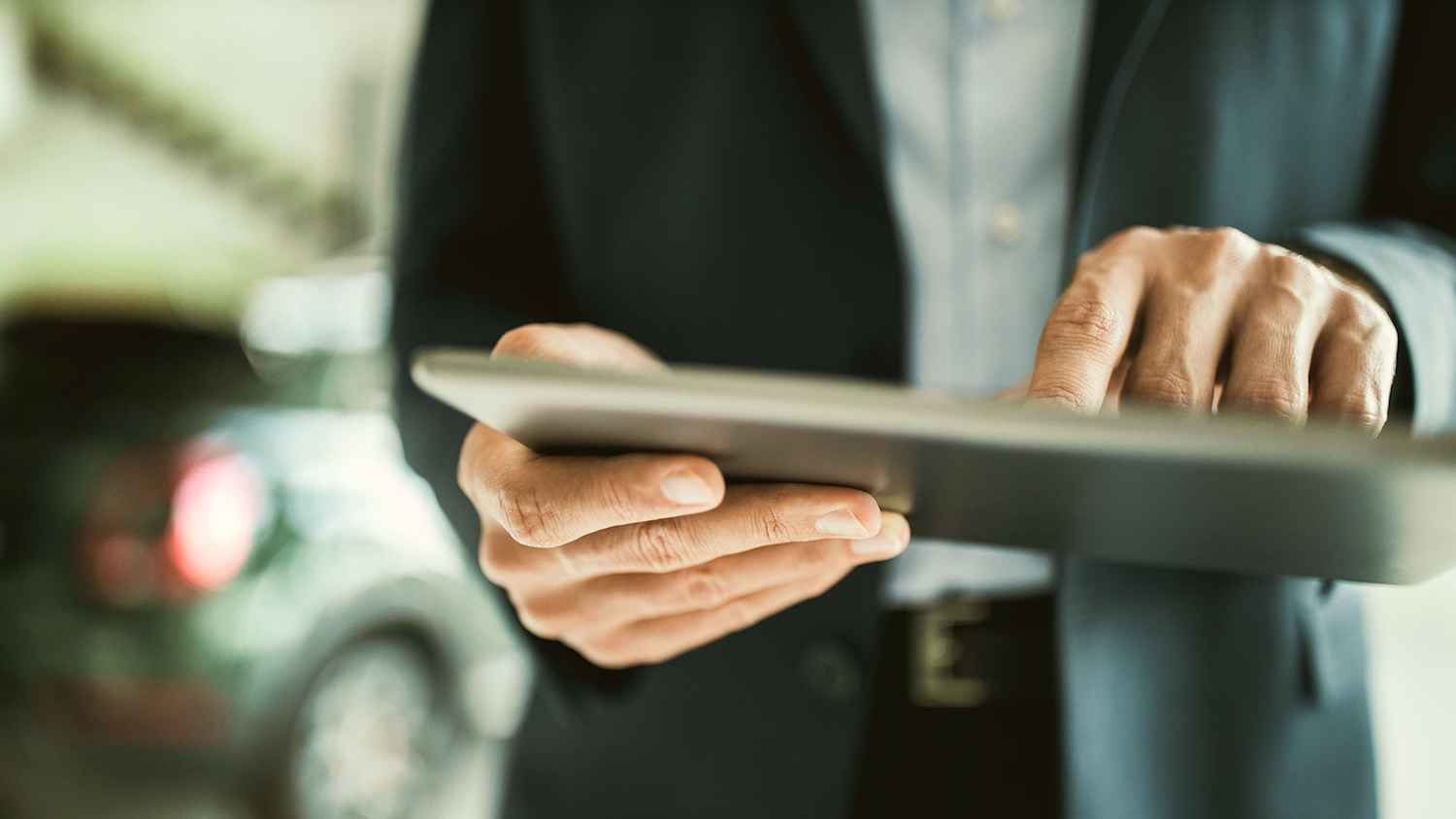 Eine Person im Anzug hält ein Tablet, um seine Autofinanzierung zu organisieren.