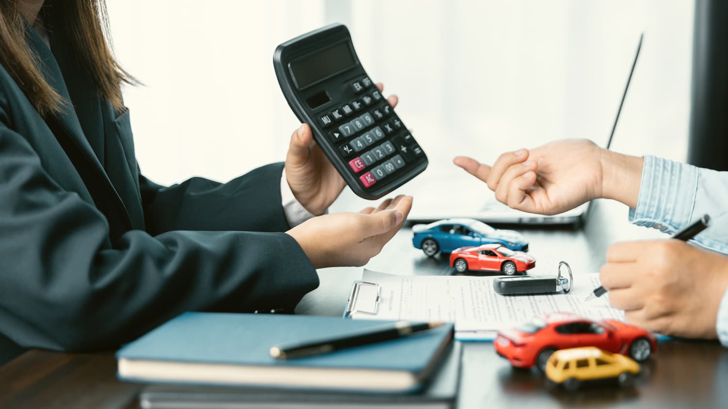 Eine Person präsentiert einen Taschenrechner, eine andere Person füllt ein Formular aus zum Auto finanzieren