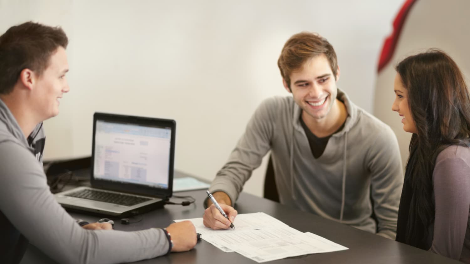 Mann und Frau sitzen an einem Tisch mit einem Mann der sie berät, ob Leasing oder Finanzierung besser ist.