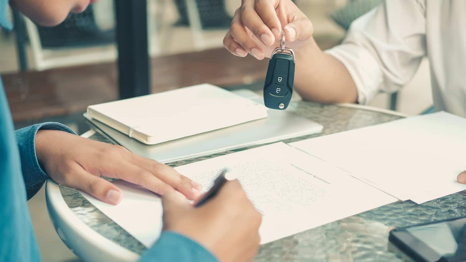 Person übergibt Schlüssel an Person, die einen Leasingvertrag unterschreibt, nachdem sie über den Leasingfaktor informiert wurde.