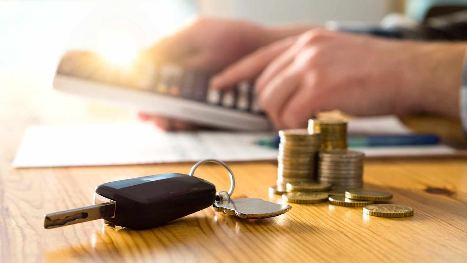 Zwei Hände berechnen eine Kfz-Versicherung mit einem Taschenrechner, daneben liegen ein Autoschlüssel und Münzen