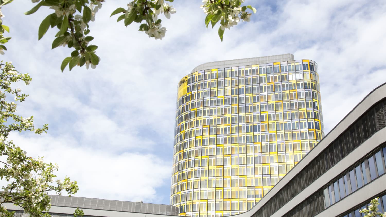 ADAC Zentrale Turm vor bayrischem weißblauem Himmel und blühendem Ast im Vordergrund