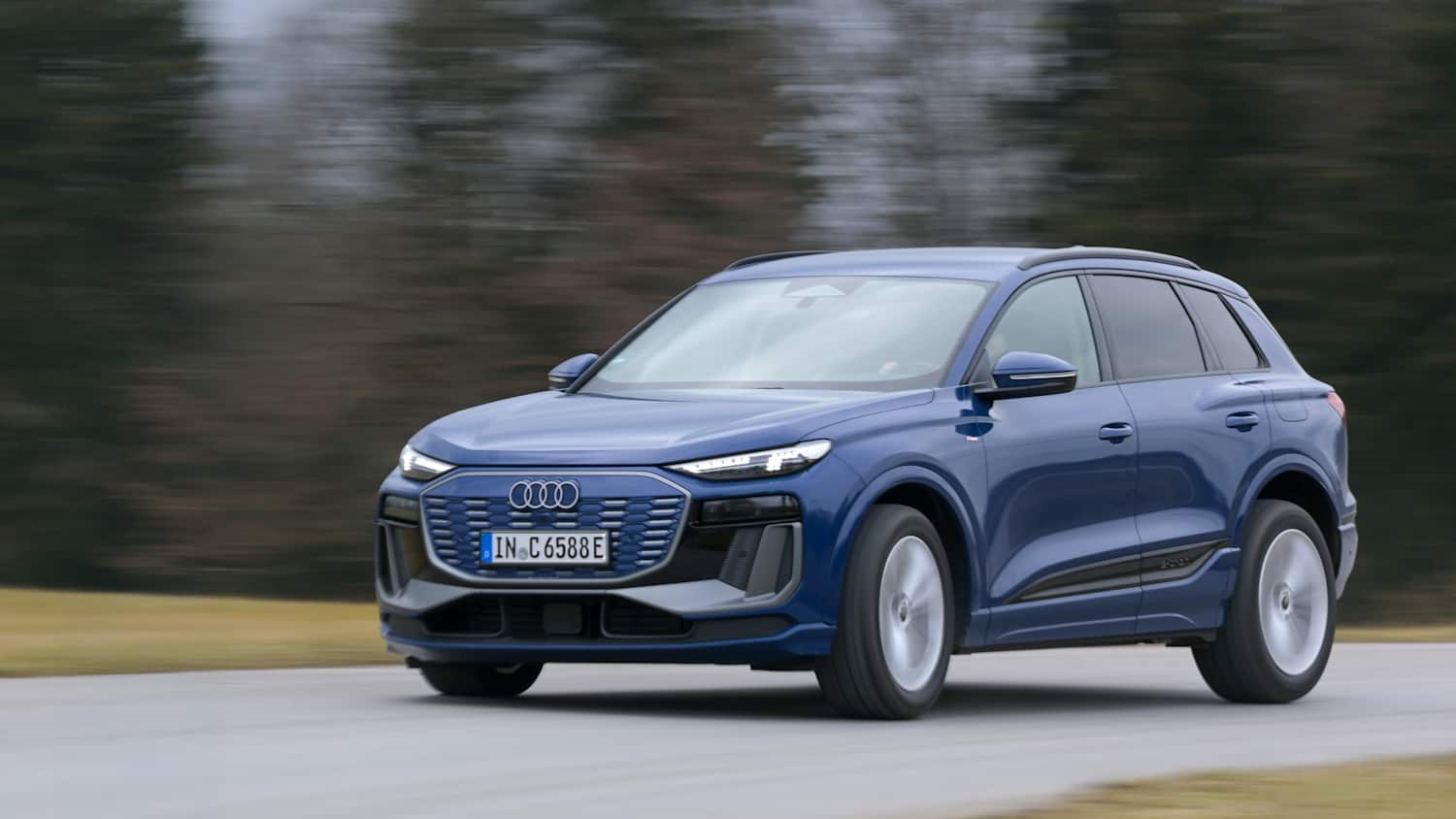 Audi Q6 e-tron in Fahrt auf einer Straße, mit verschwommenem Hintergrund bei bewölktem Wetter.