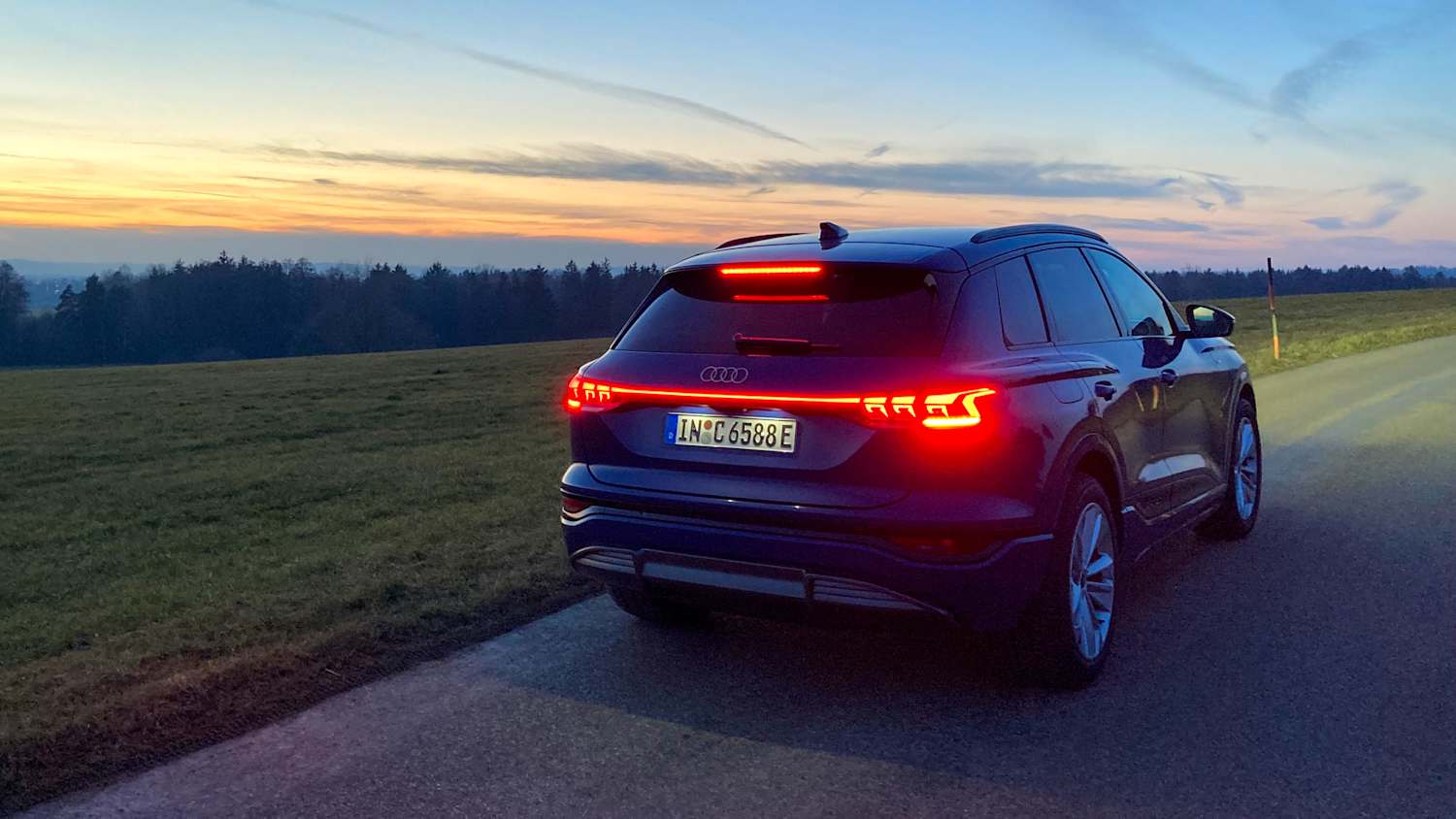 Rückleuchten eines Audi Q6 e-tron, rot leuchtend bei Dämmerung.