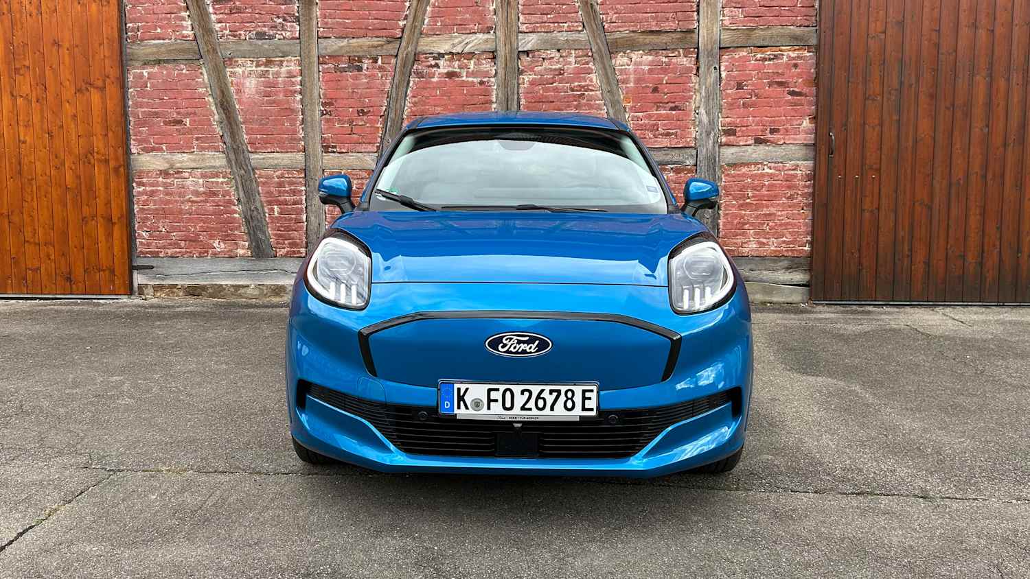 Frontansicht eines blauen Ford Puma Gen-E, geparkt vor einer Backsteinwand