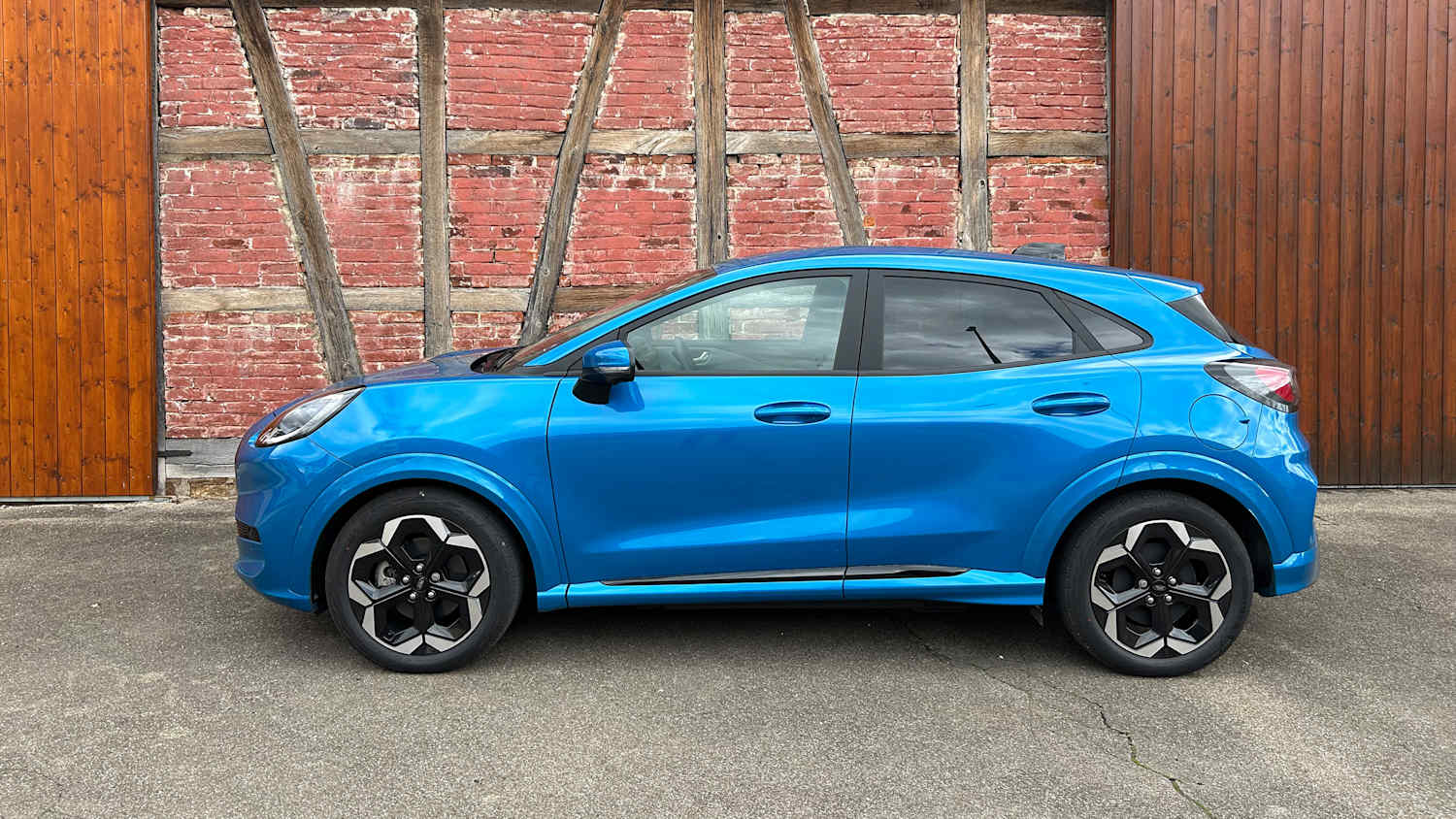 Seitenansicht eines blauen Ford Puma Gen-E, geparkt vor einer Backsteinwand.