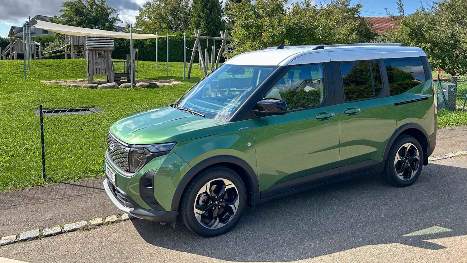 Ford Tourneo E-Courier stehend neben einer Wiese, Seitenansicht.