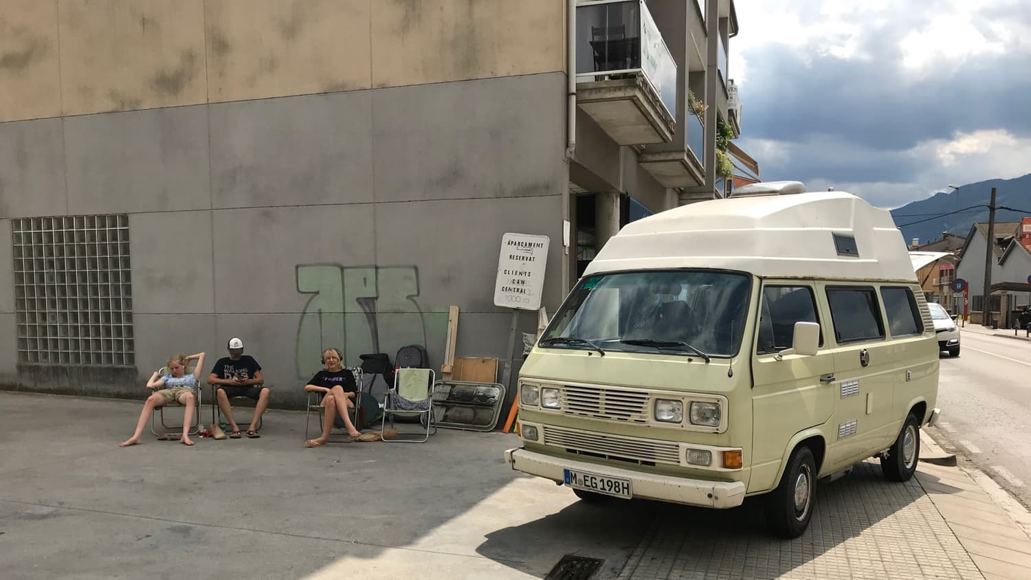 Eine Familie sitzt auf Campingstühlen auf einer Straße neben ihrem VW-Bus