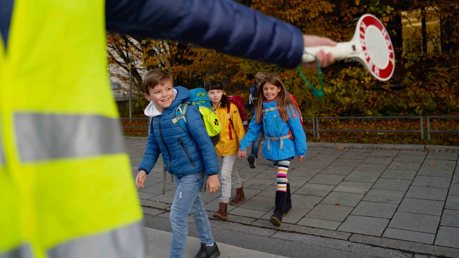 Schulkinder beim überqueren einer Straße mit Hilfe eines Schulweghelfers
