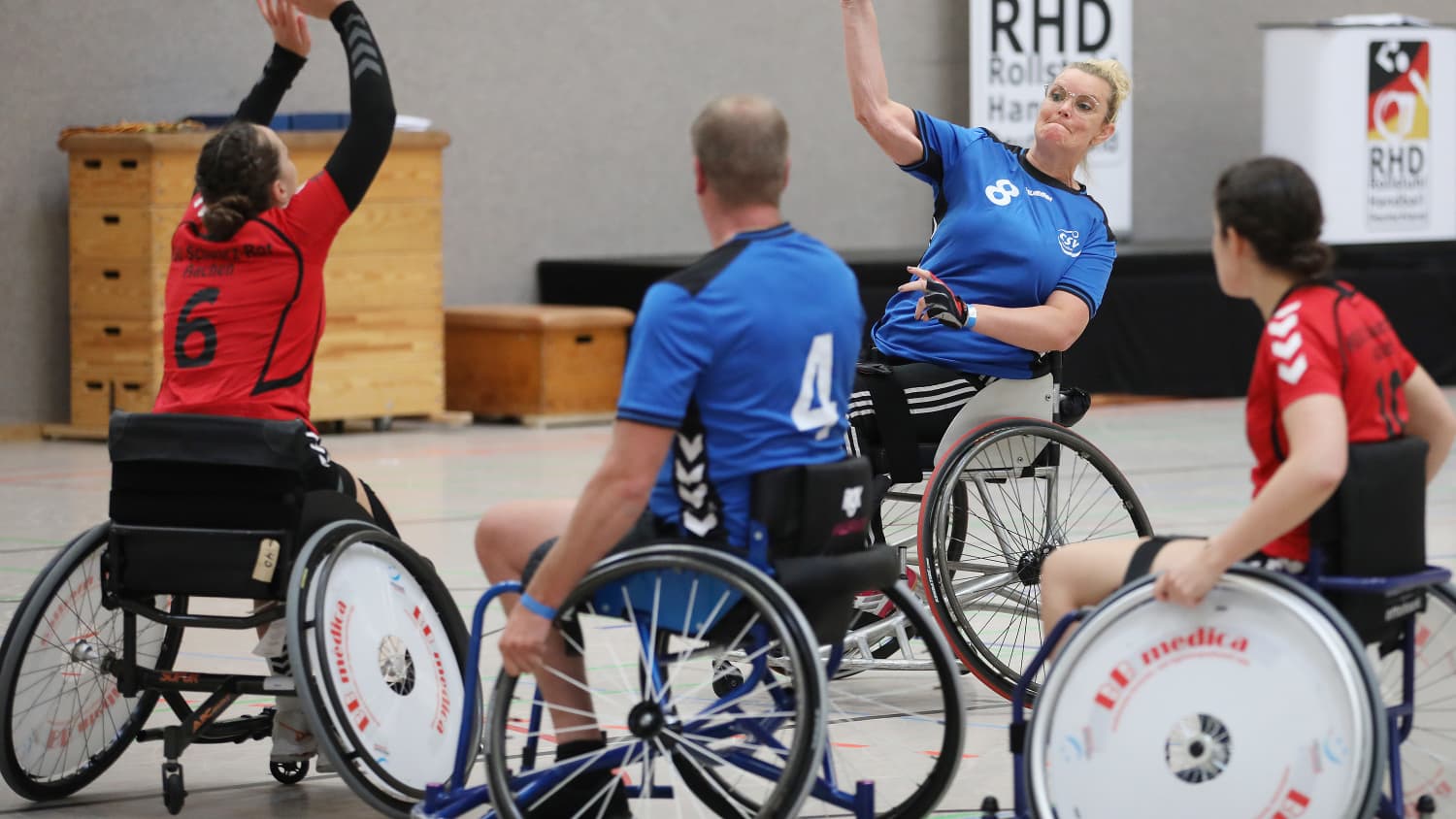 Vier Rollstuhlfahrer spielen Rolli-Handball in einer Halle