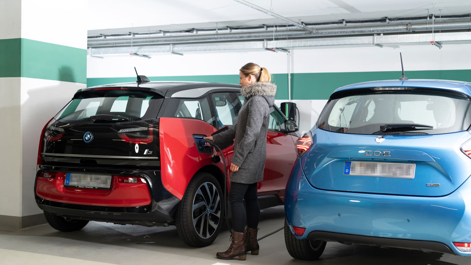 Frau lädt Ihren roten BMW  i3 in der Tiefgarage eines Mehrfamilienhauses