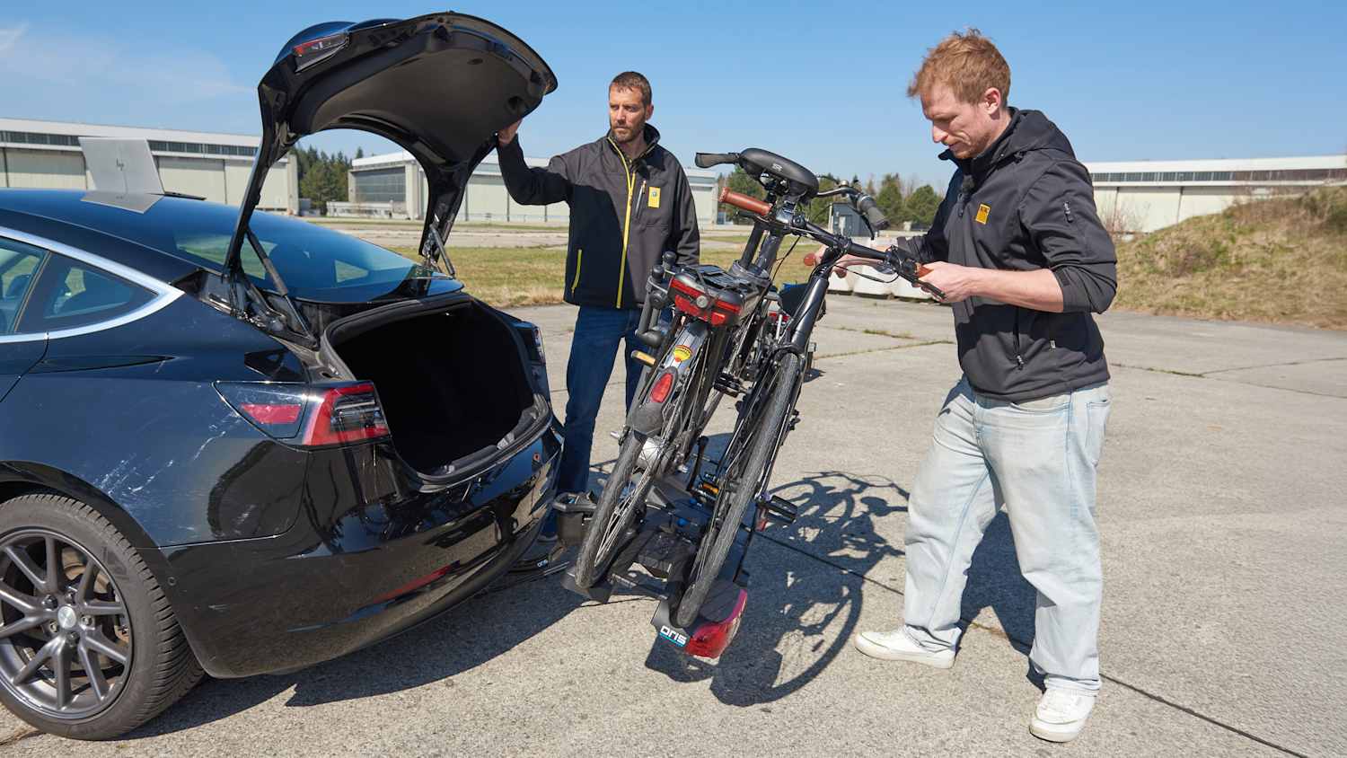 Zwei ADAC Ingenieure befestigen einen Fahrradheckträger an einem Auto