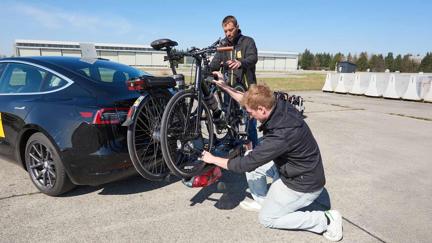 Zwei ADAC Ingenieure befestigen einen Fahrradheckträger an einem Auto