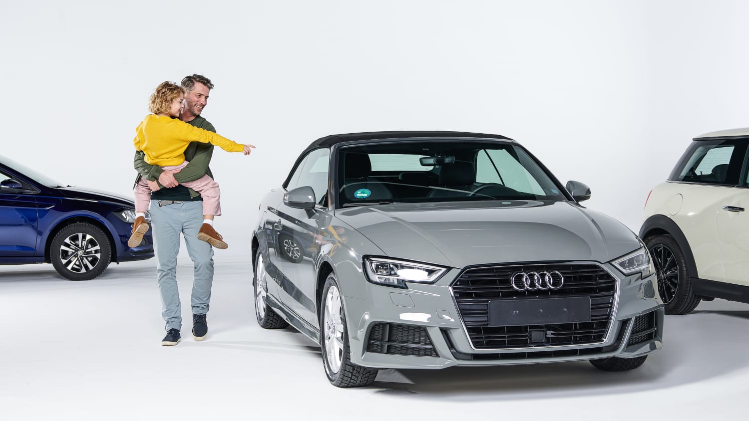 Vater trägt seine Tochter, die auf einen grauen Audi zeigt
