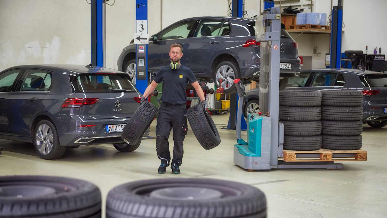 Ein Mann trägt zwei Autoreifen in einer Autowerkstatt