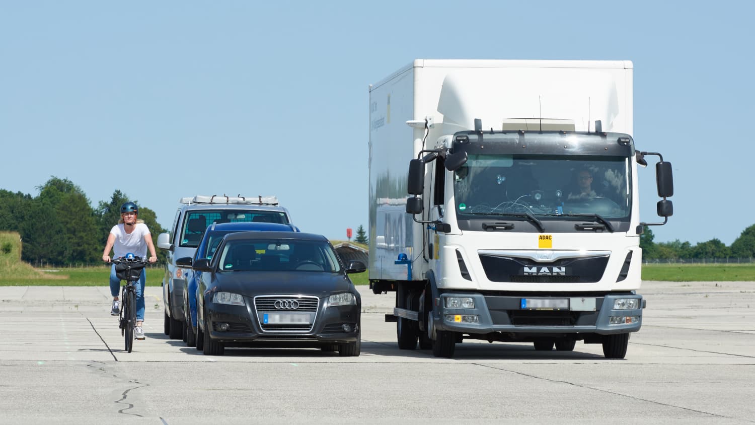 LKW und Radfahrerin neben einer Reihe von geparkten Autos