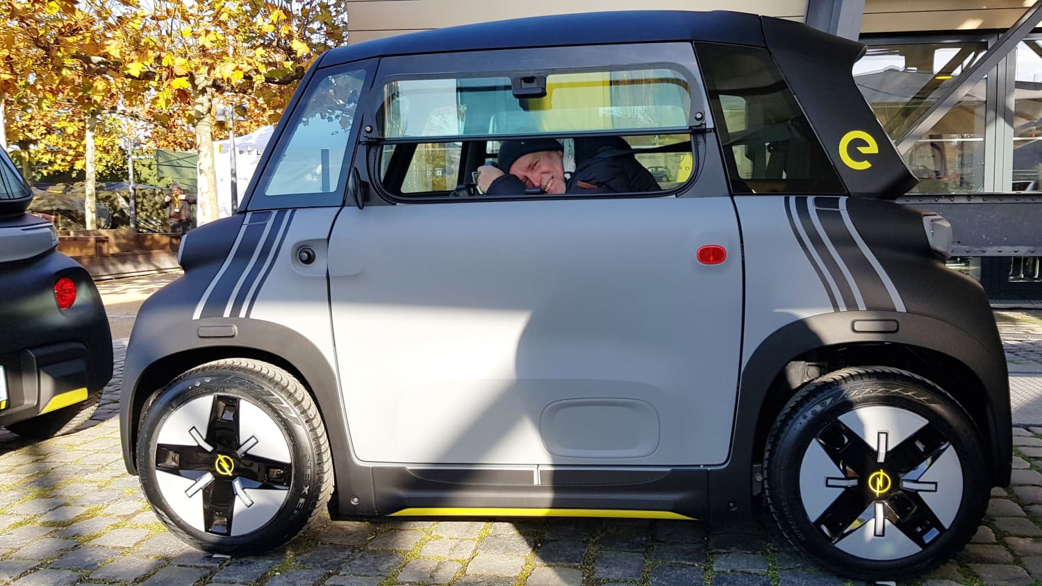 ADAC Redakteur Wolfgang Rudschies sitzt an einem sonnigen Hersttag in dem kleinen Opel Rocks e und blickt aus dem Seitenfenster, das man nach oben aufklappen kann