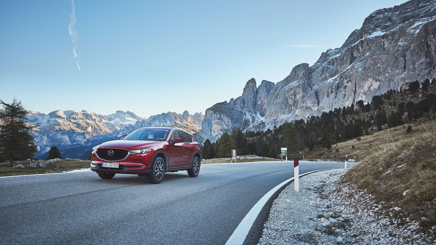 Ein rotes Auto fährt auf einer Passstrasse vor einem Bergpanorama