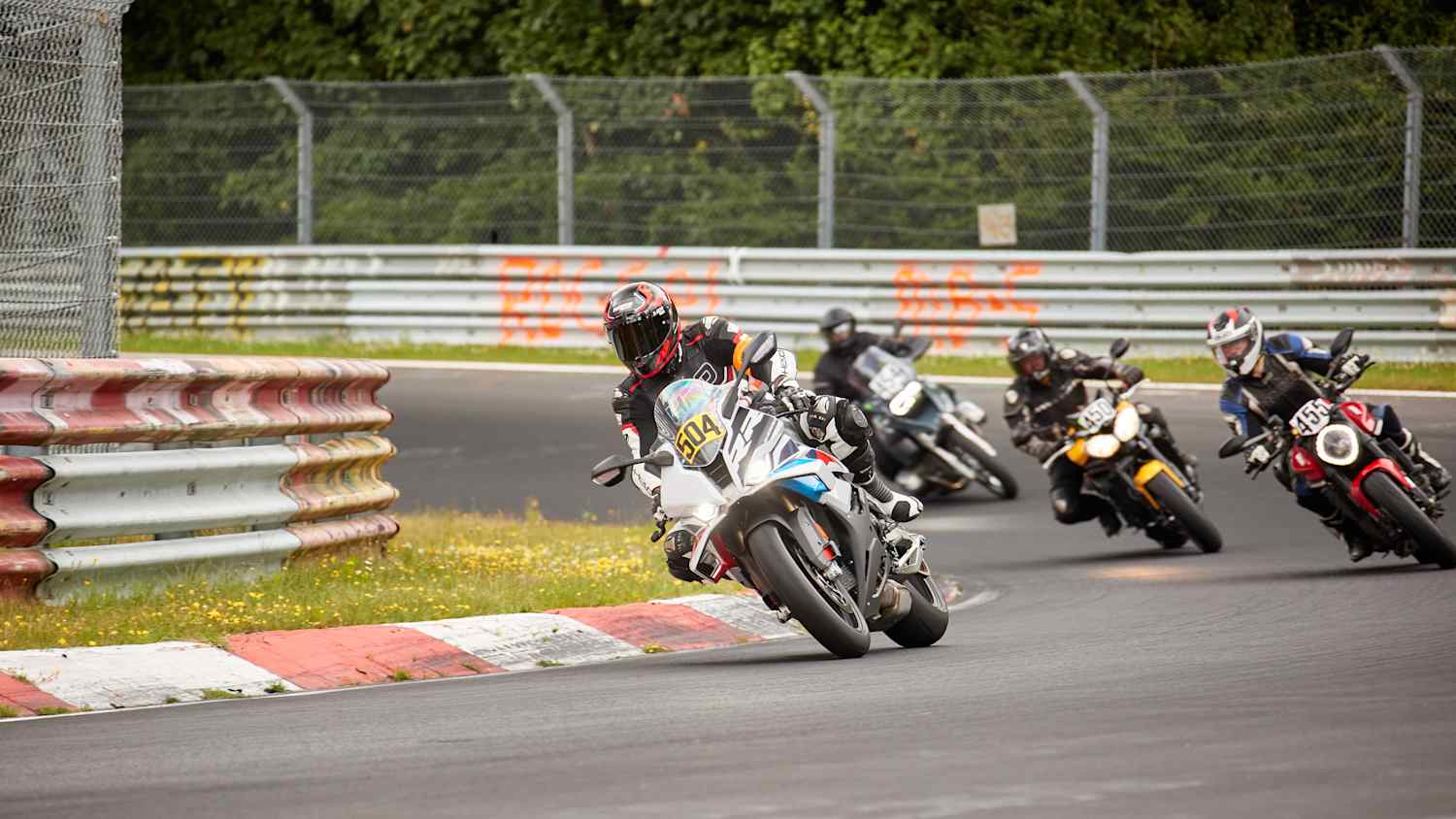 Motorradfahrer fahren auf einer Rennstrecke, während Zuschauer am Rand zuschauen.