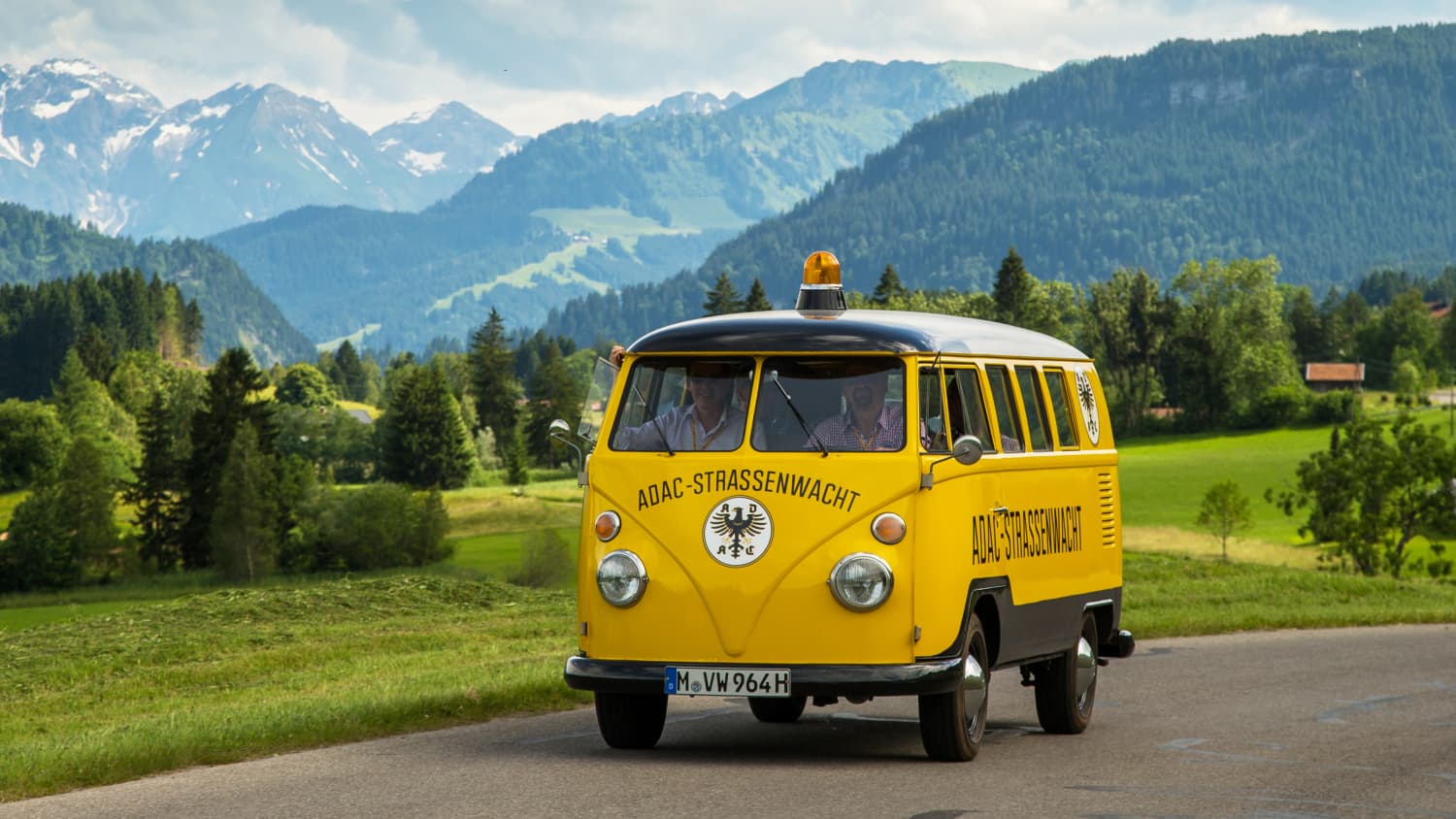 Alter T1 Bulli der ADAC Strassenwacht fährt auf einer Strasse vor Bergpanorama
