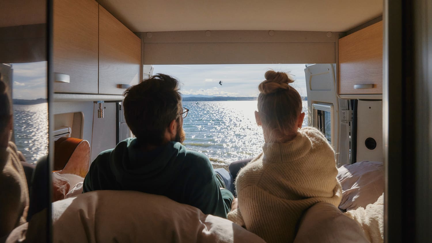 Ein Pärchen liegt in seinem Wohnmobil und blickt auf den See