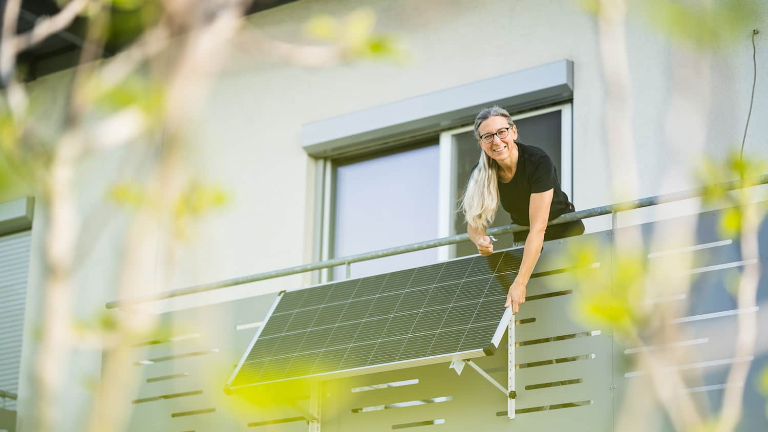 Eine Frau justiert ein Solarpanel an ihrem Balkon