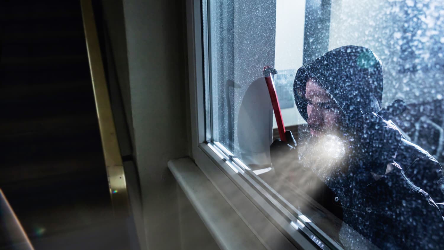 Ein Einbrecher leuchtet mit einer Taschenlampe durch ein Fenster