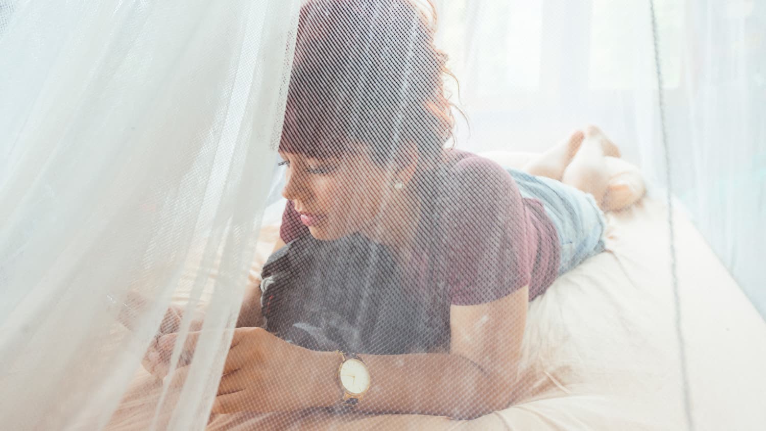 Eine Frau sitz auf dem Bett unter Mückennetz