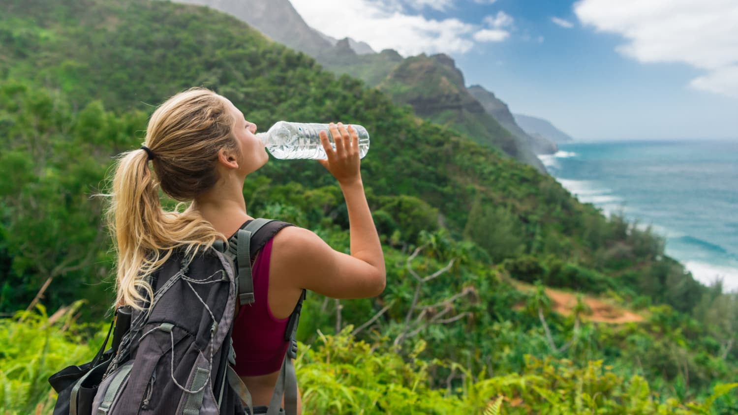 Frau trinkt auf einer Wanderung am Meer aus einer Flasche