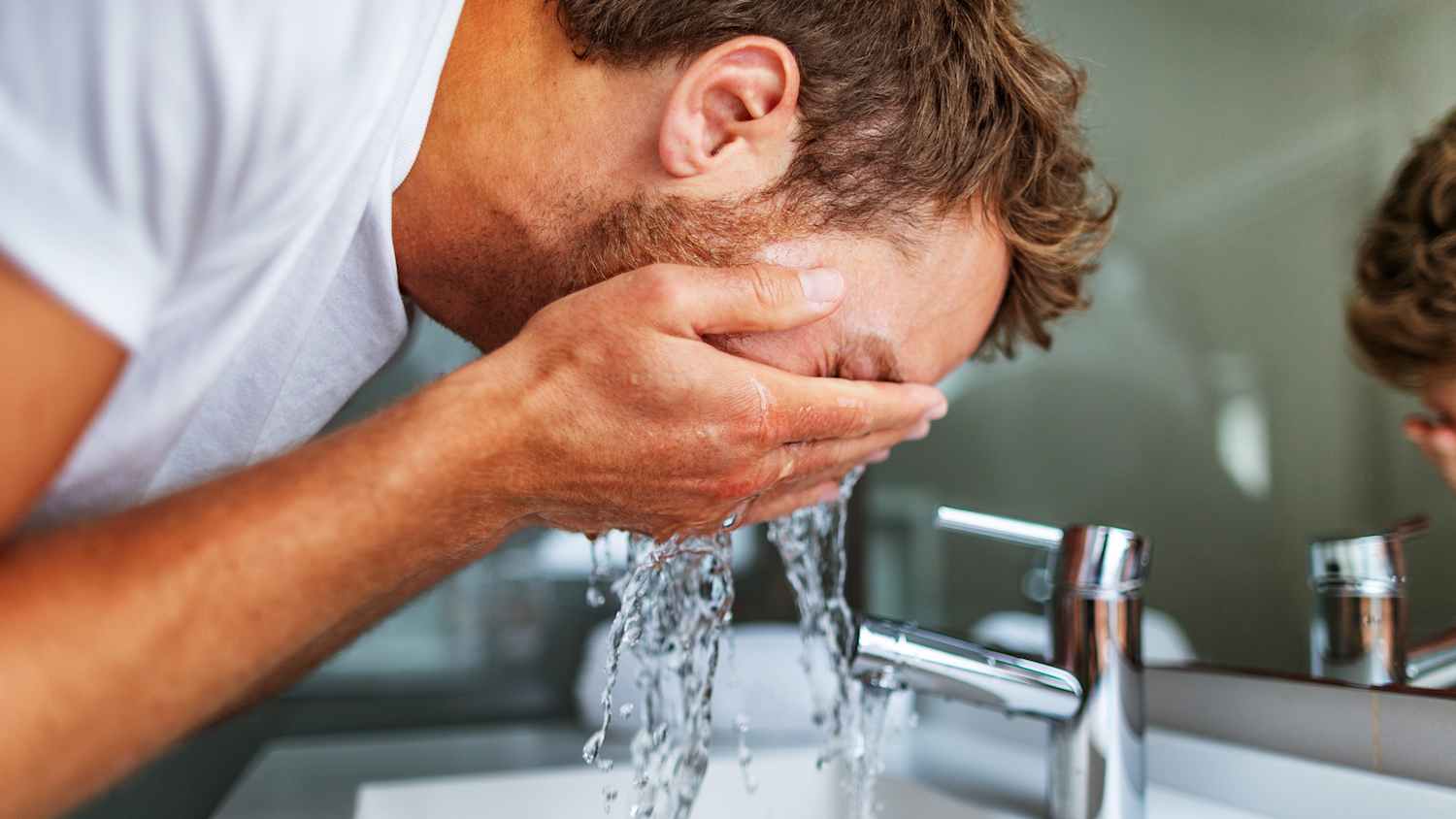 Ein Mann welcher sich mittels eines Warmwasserspeichers, geheizten Wassers das Gesicht wäscht