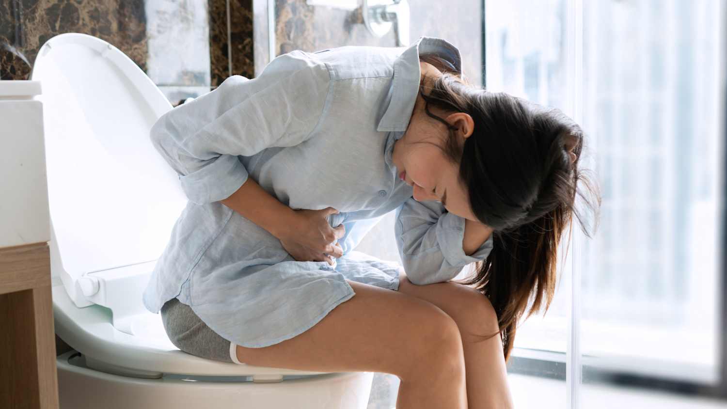 Eine Frau sitzt mit Bauchkrämpfen auf der Toilette