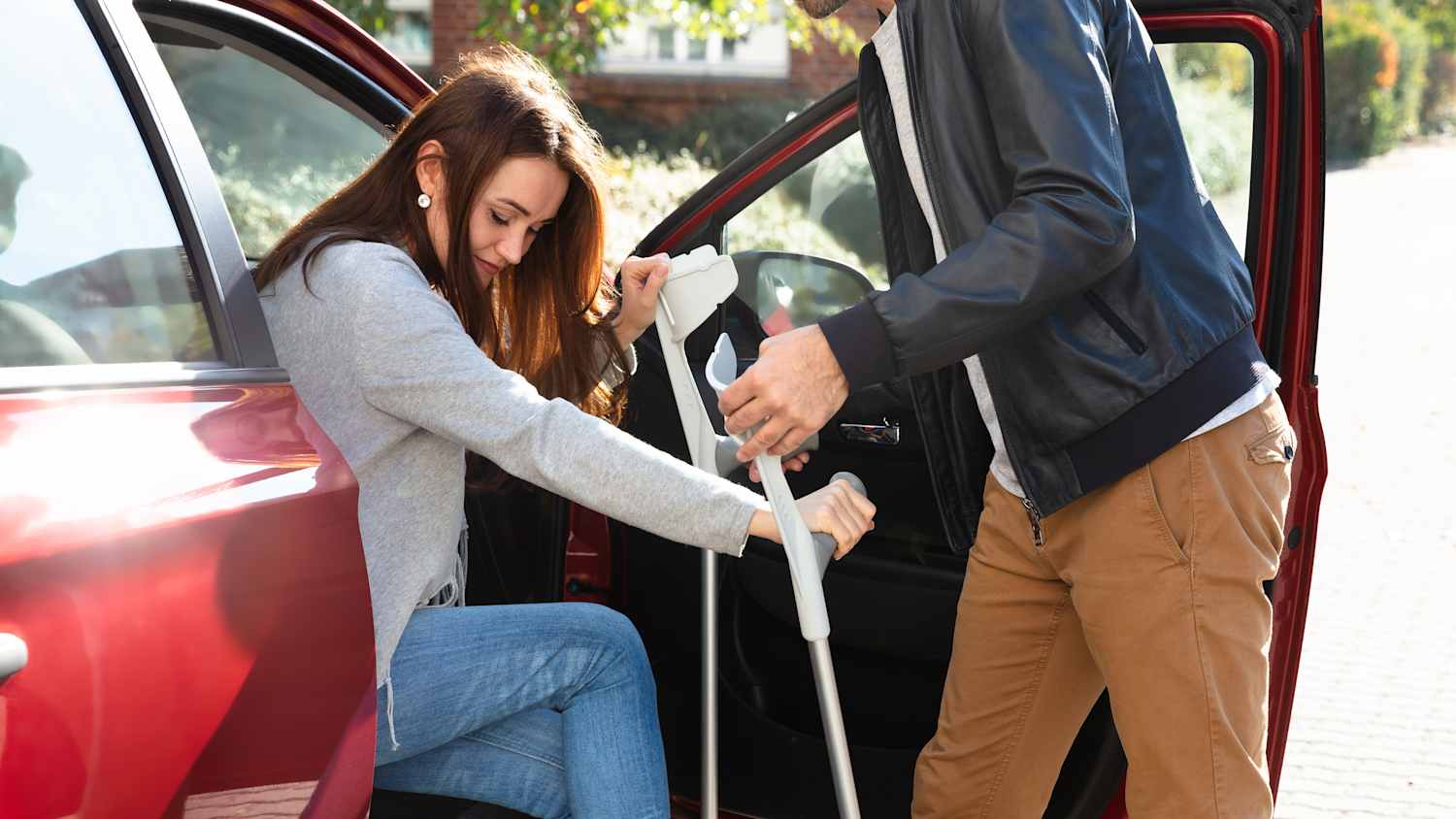 Ein Mann hilft einer Frau mit Krücken ins Auto