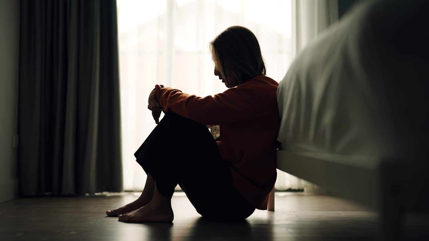 Eine junge frau mit Depressionen sitzt im Schlafzimmer auf dem Boden.