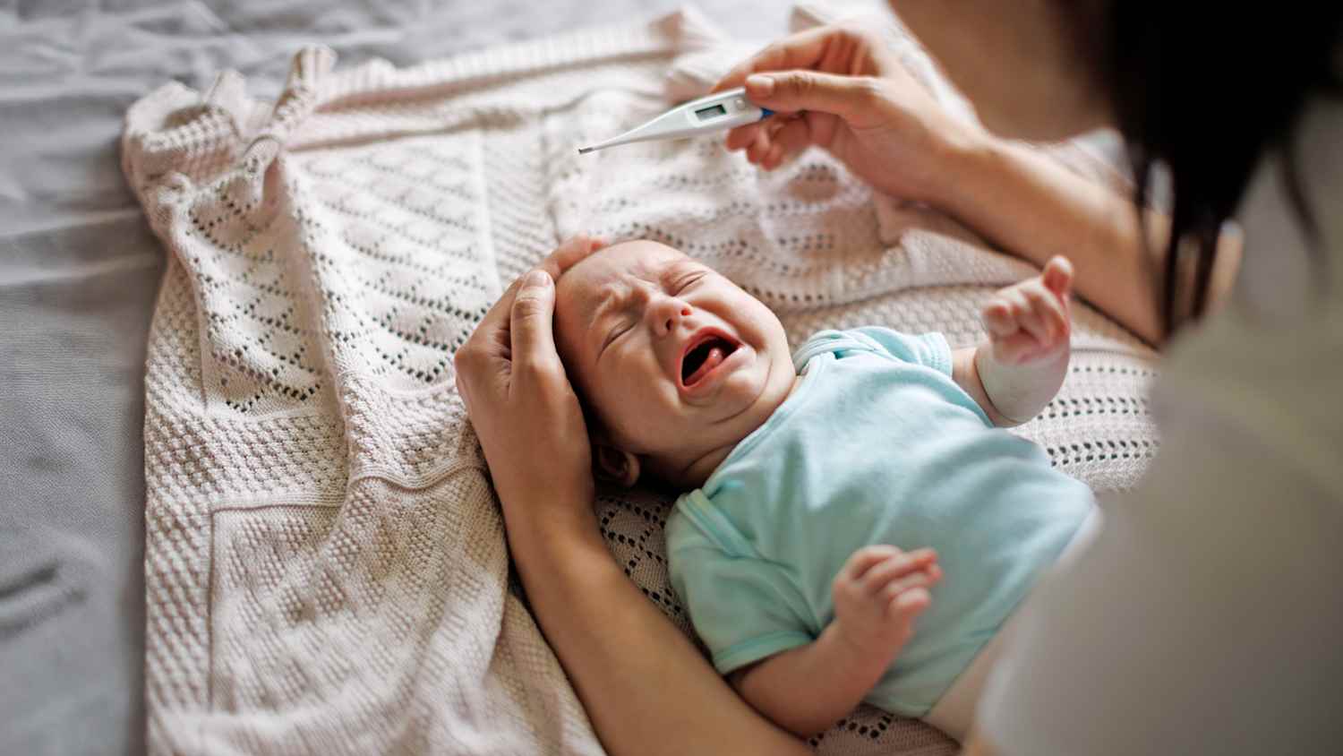 Eine Mutter misst ihrem weinenden Kind die Temperatur