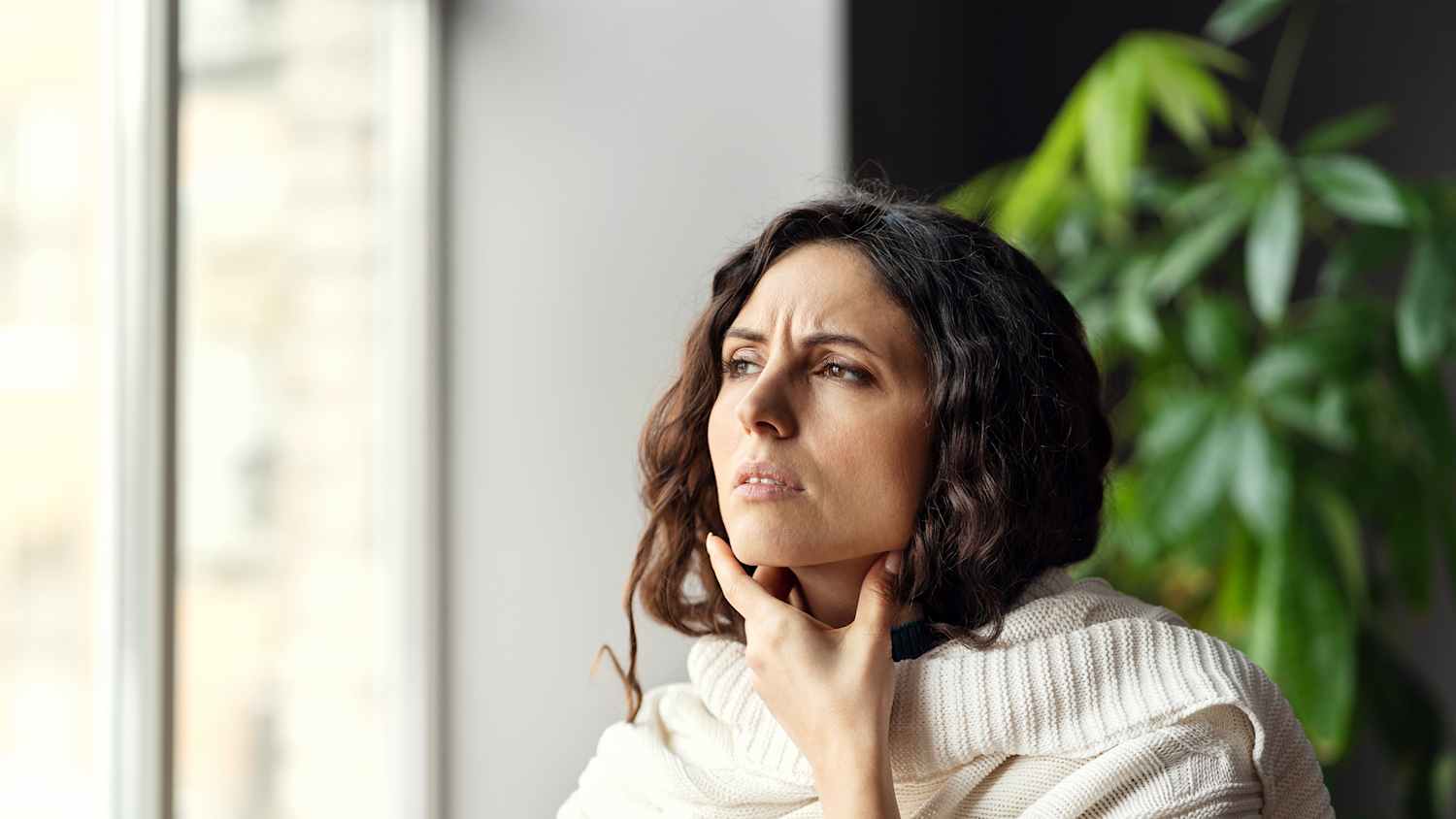 Eine Frau die sich zu Hause an den Hals lässt und ihre Lymphknoten abtastet.