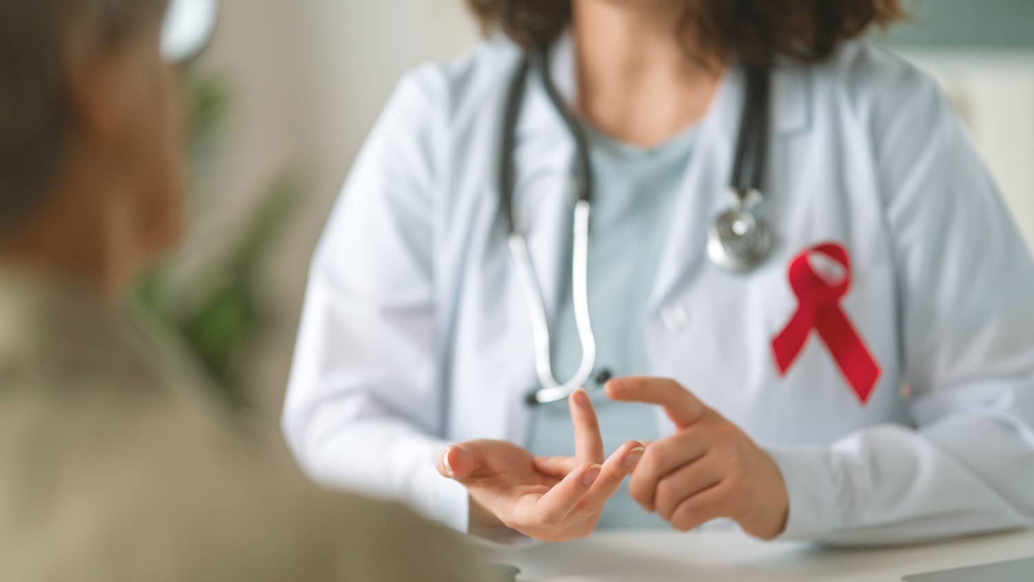 Eine Ärztin im Patientengespräch an ihrem Kittel ist eine rote HIV Schleife