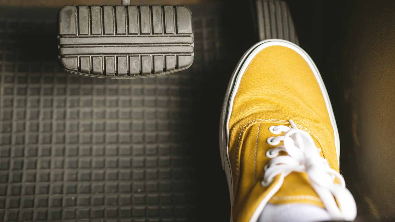 Ein Fuß mit einem gelben Segelschuh auf dem Gaspedal eines Autos