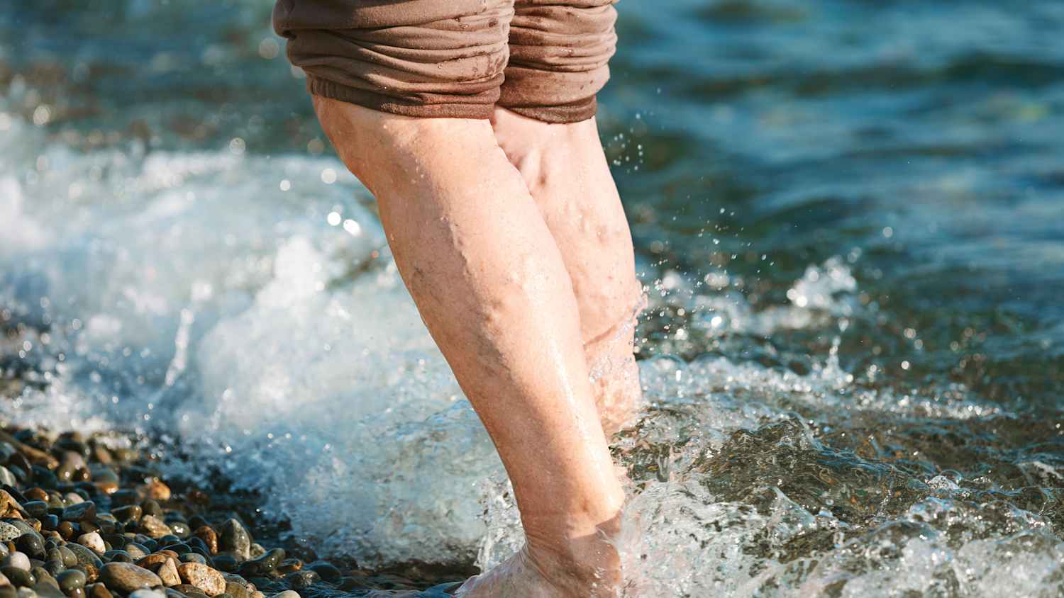 Jemand kühlt seine Beine mit offensichtlichen Krampfadern im Meer