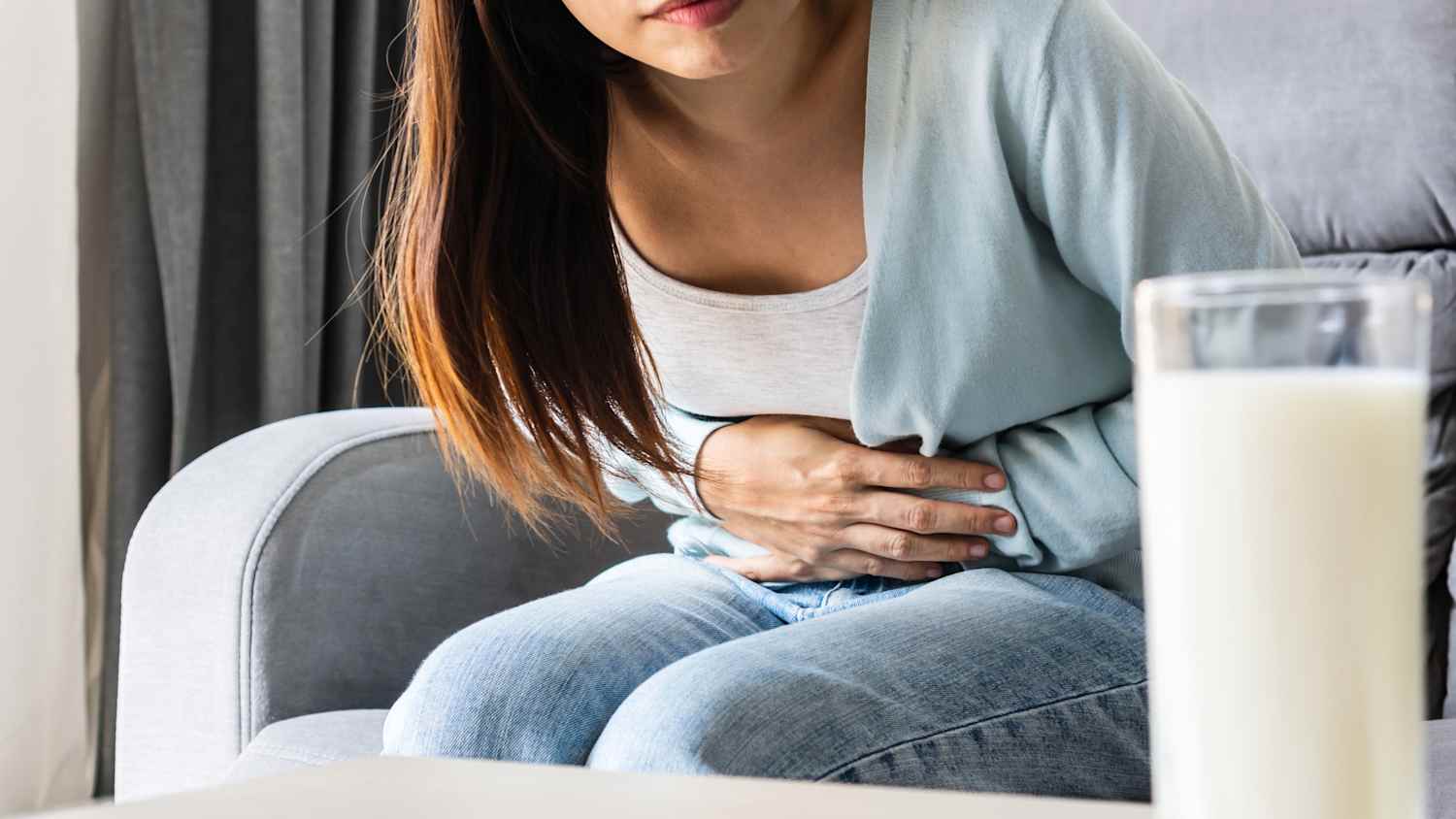 Eine Frau sitzt auf dem Sofa und hält sich den Bauch vor Schmerzen weil sie Milch getrunken hat