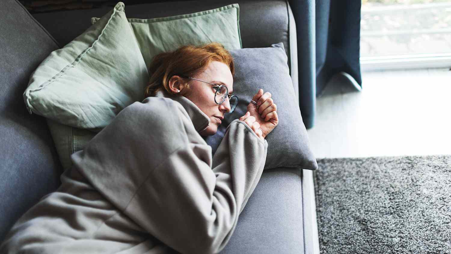 eine erwachsene Frau liegt erschöpft und betrübt auf dem Sofa